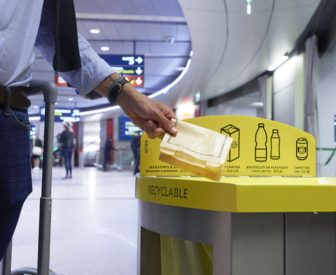 Un homme jette un sachet en papier dans une poubelle de tri sélectif dans un aéroport
