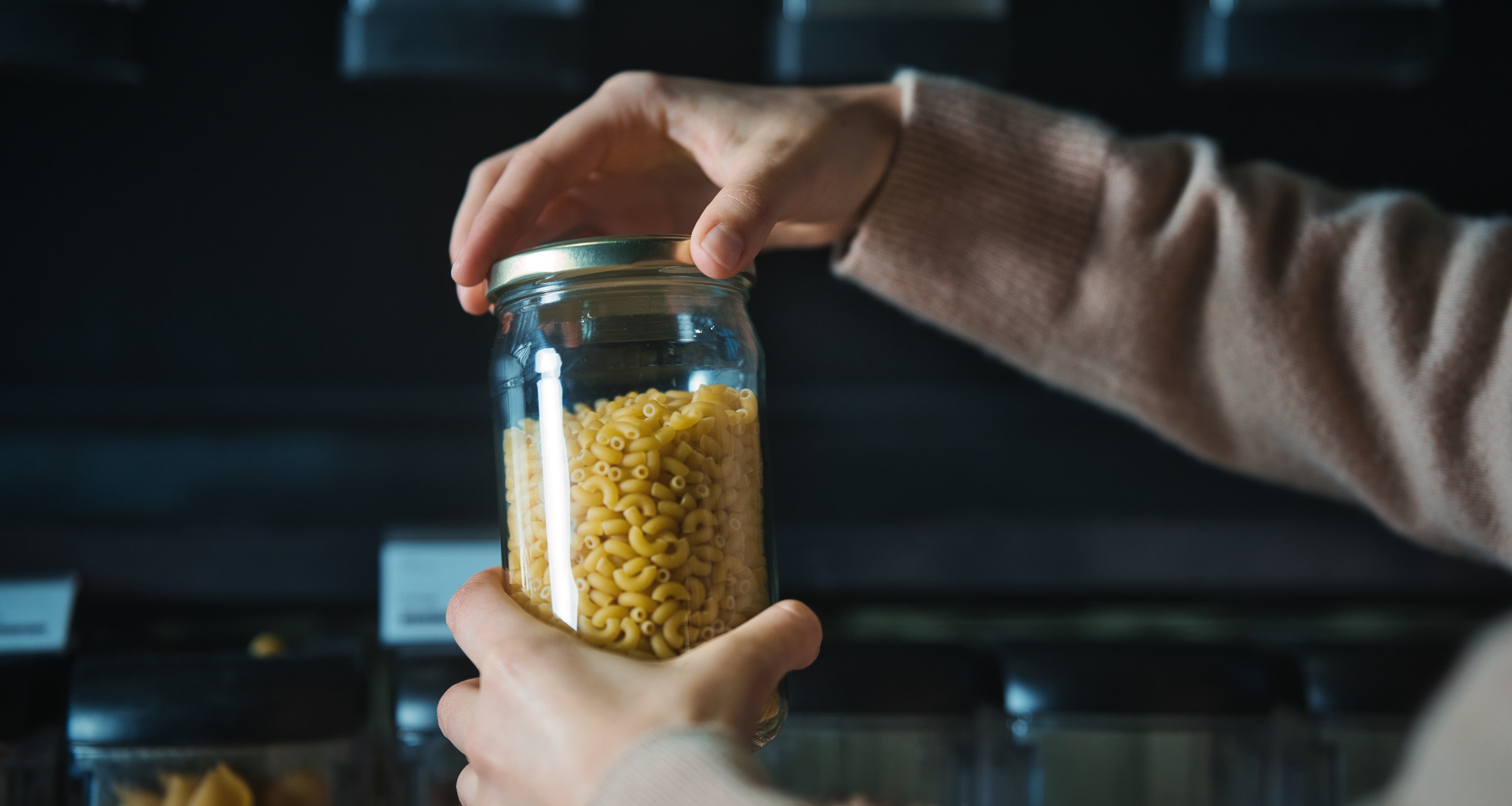 Personne tenant un bocal en verre rempli de pÃ¢tes en vrac 
