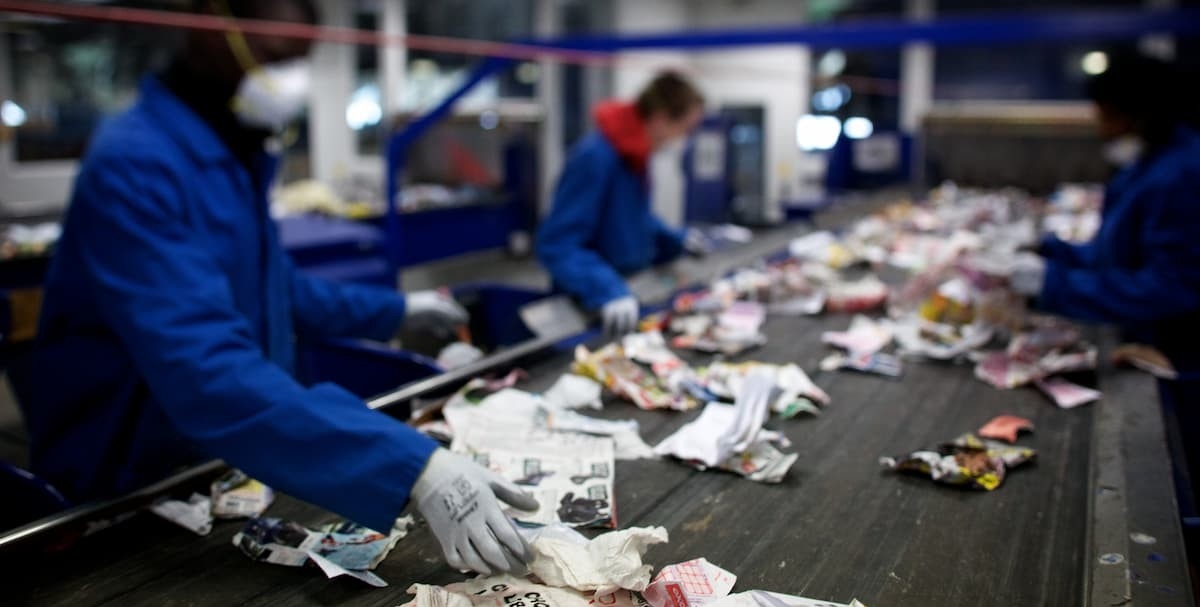 EmployÃ©s triant les dÃ©chets sur un tapis de tri dans centre de recyclage